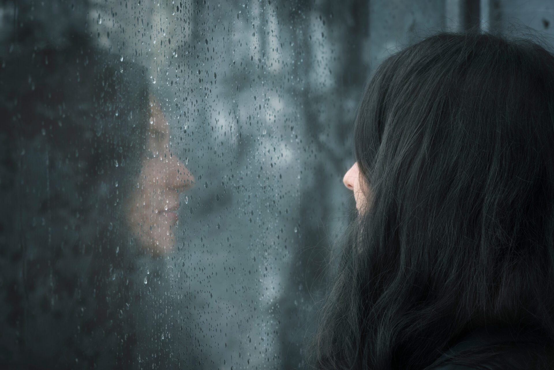 Profile image of a young brunette woman with closed eyes thinking  in front of rainy window